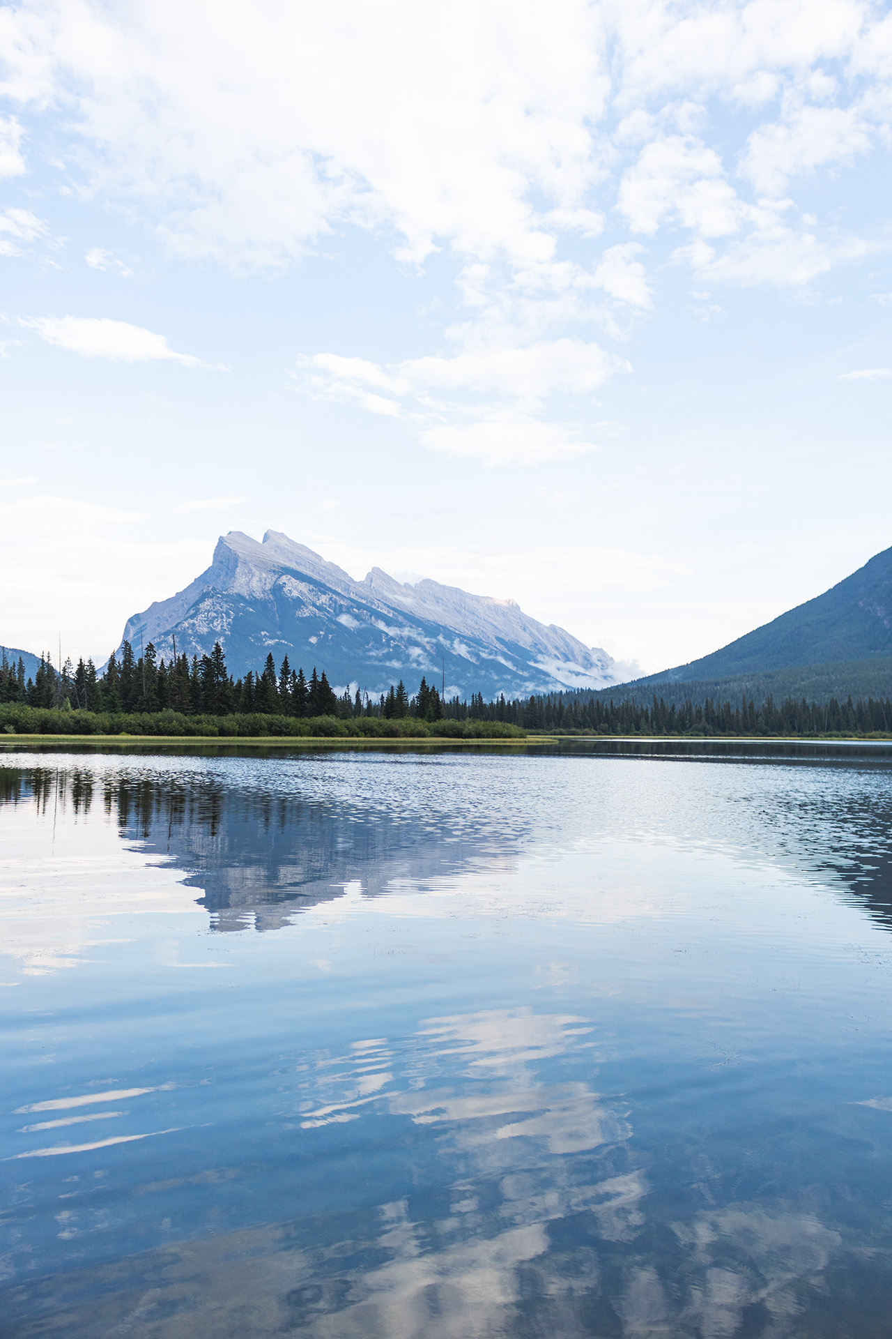 Calm lake with a large rocky slanted mountain far behind it.